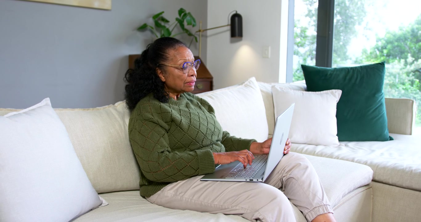 Senior African American woman resuming work on silver laptop at home in green sweater pausing