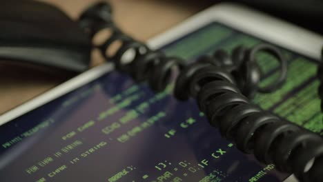 black phone on desk with code running on a screen in the background