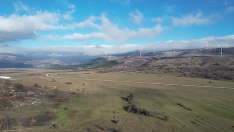 Beautiful-aerial-shot-of-Croatian-landscape-with-wind-turbines-generating-renewable-energy-in-the-background-and-an-empty-road,-in-the-region-of-Lika-in-Croatia,-Europe