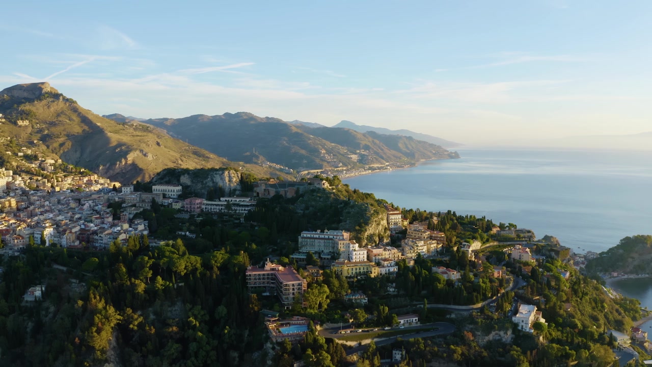 Asentamiento urbano al pie de las montañas rocosas en Sicilia. Toma aérea orbital con dron sobre la histórica ciudad de Taormina.