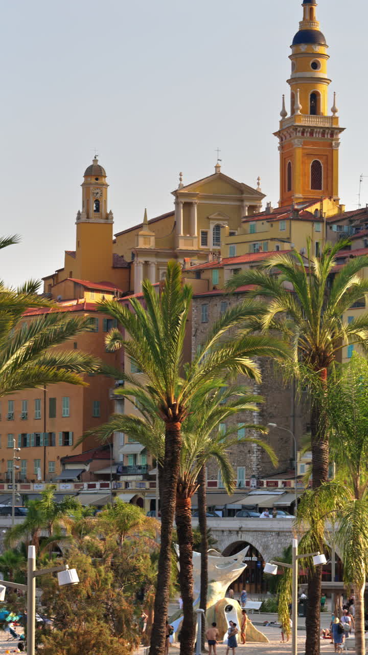 View of palm trees with the colourful buildings in Menton, France on the background. Vertical