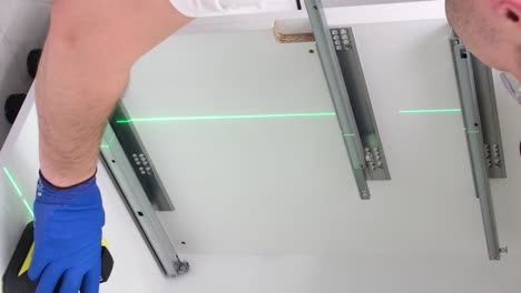 a young craftsman in a black cap uses an electronic level to install kitchen furniture