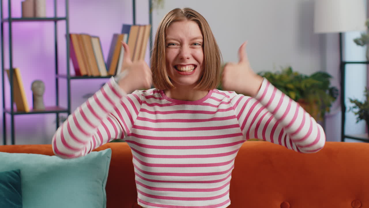 Happy young woman looking approvingly at camera showing thumbs up like positive sign good news