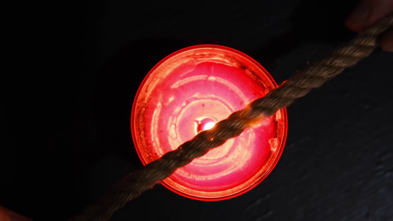 quemando una cuerda de yute en el fuego de una vela para el ritual shibari