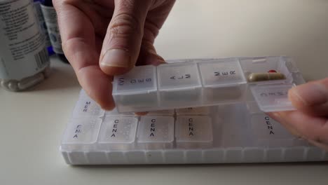 Hand placing pills in a weekly supplements organizer, health care and routine at home