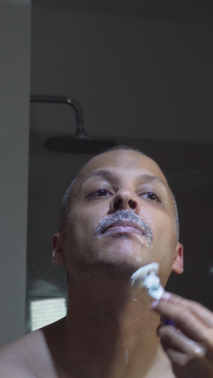Hombre afeitándose la cara con una maquinilla de afeitar en el baño