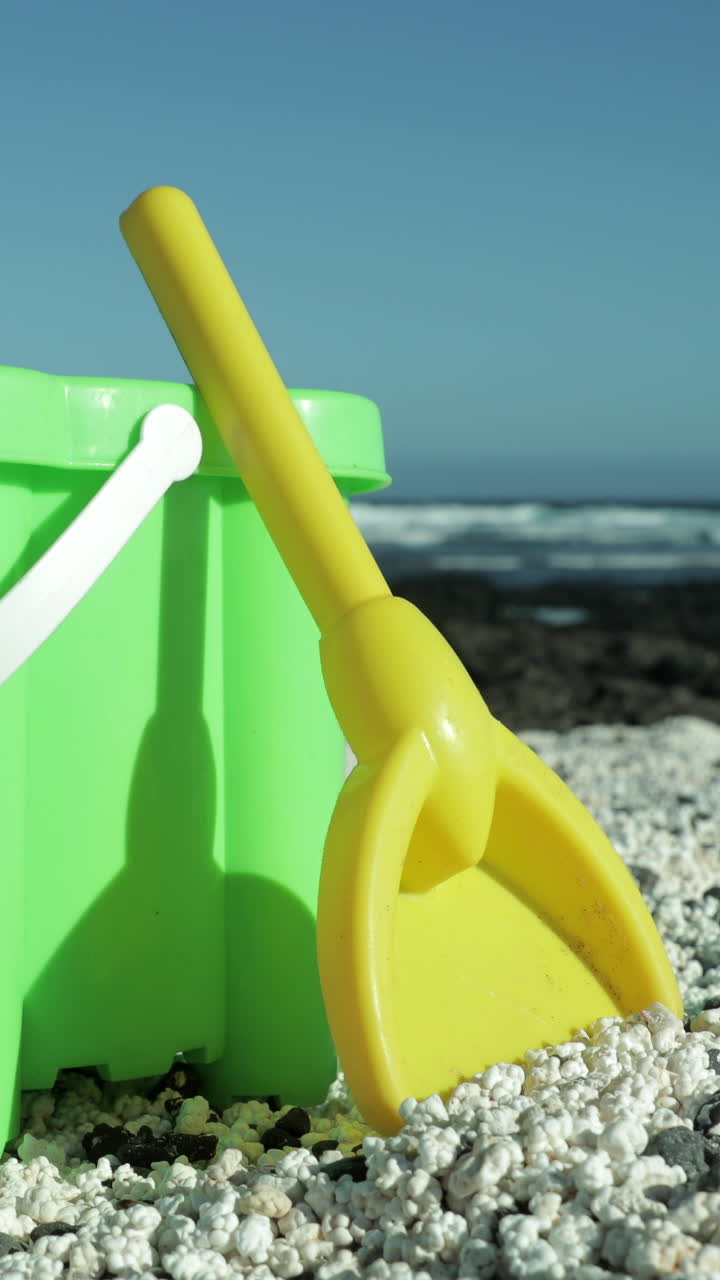 cubo de plástico y pala en una playa de arena negra con el océano en vertical