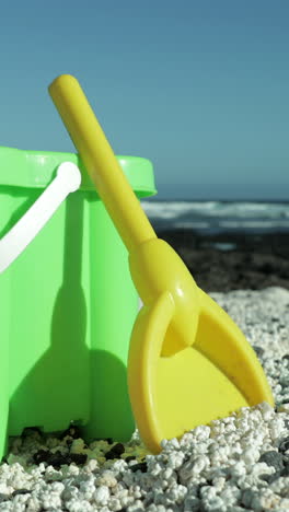 plastic-bucket-and-spade-on-a-black-sand-beach-with-the-ocean-in-vertical