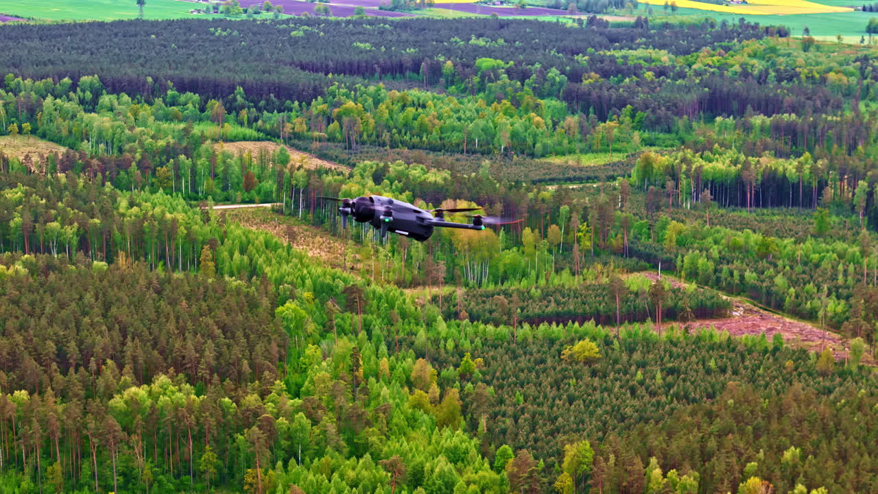 Military drone flying low over dense green forest in springtime aerial view