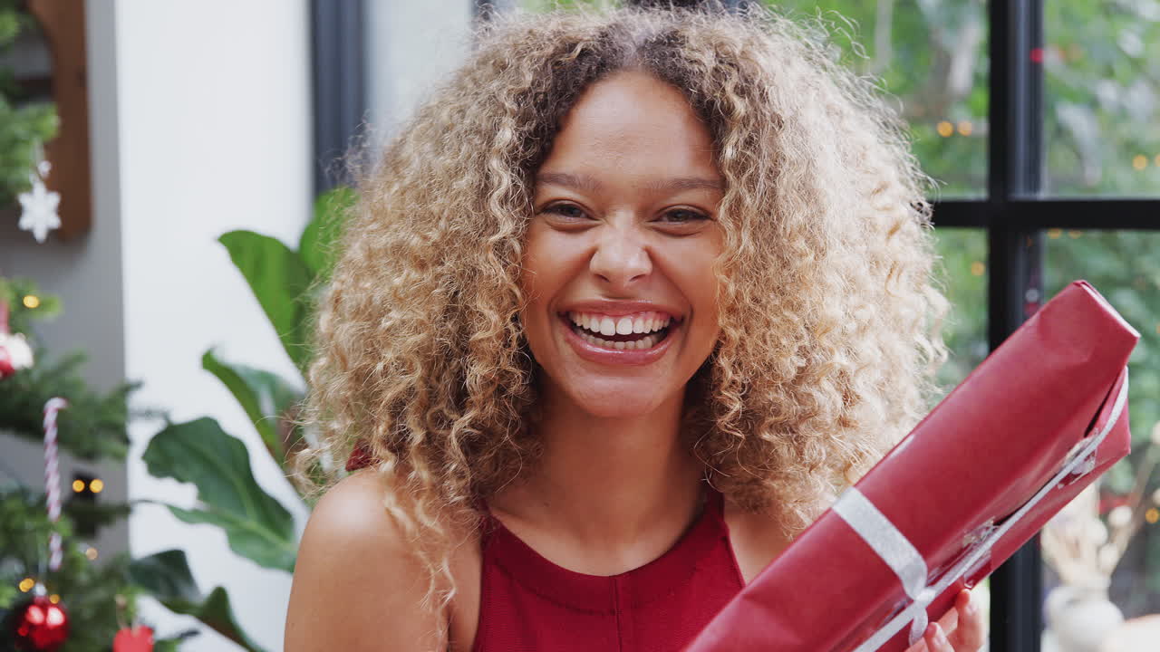 retrato de una mujer por un árbol sacudiendo el regalo de navidad tratando de adivinar el contenido