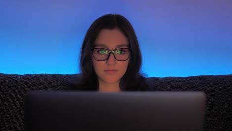 mujer joven con anteojos trabajando hasta tarde en una computadora portátil en la comodidad de su habitación