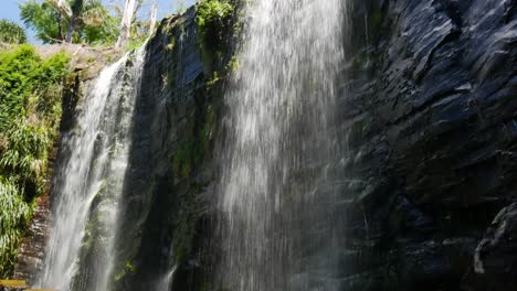 water falling down the steep edge of cliff during sunny day - kerikeri waterfalls,new zealand