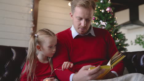 unteransicht von vater und tochter, die auf dem sofa neben dem weihnachtsbaum sitzen 1