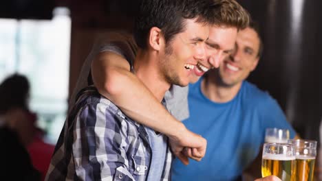felices aficionados al deporte caucásicos abrazándose y bebiendo en el bar, riendo y sonriendo