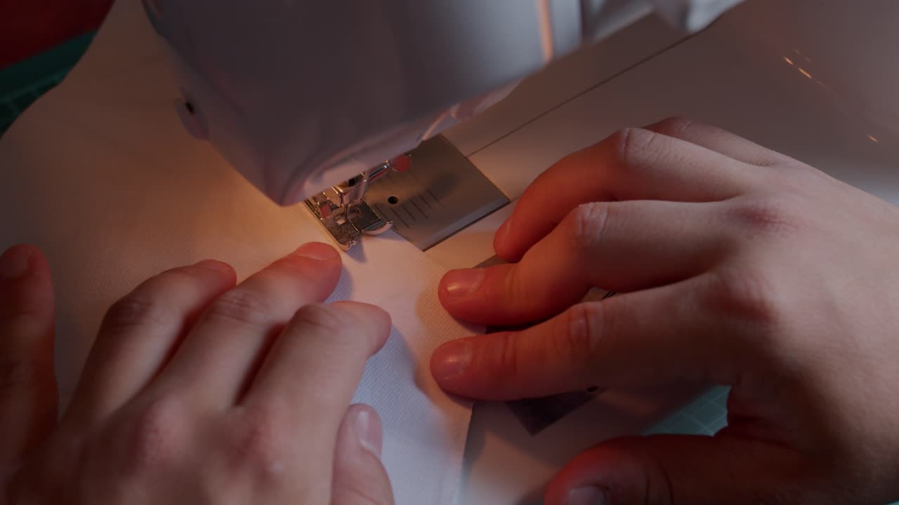 Top front view of sewing machine pulling fabric through guided by operator's hands