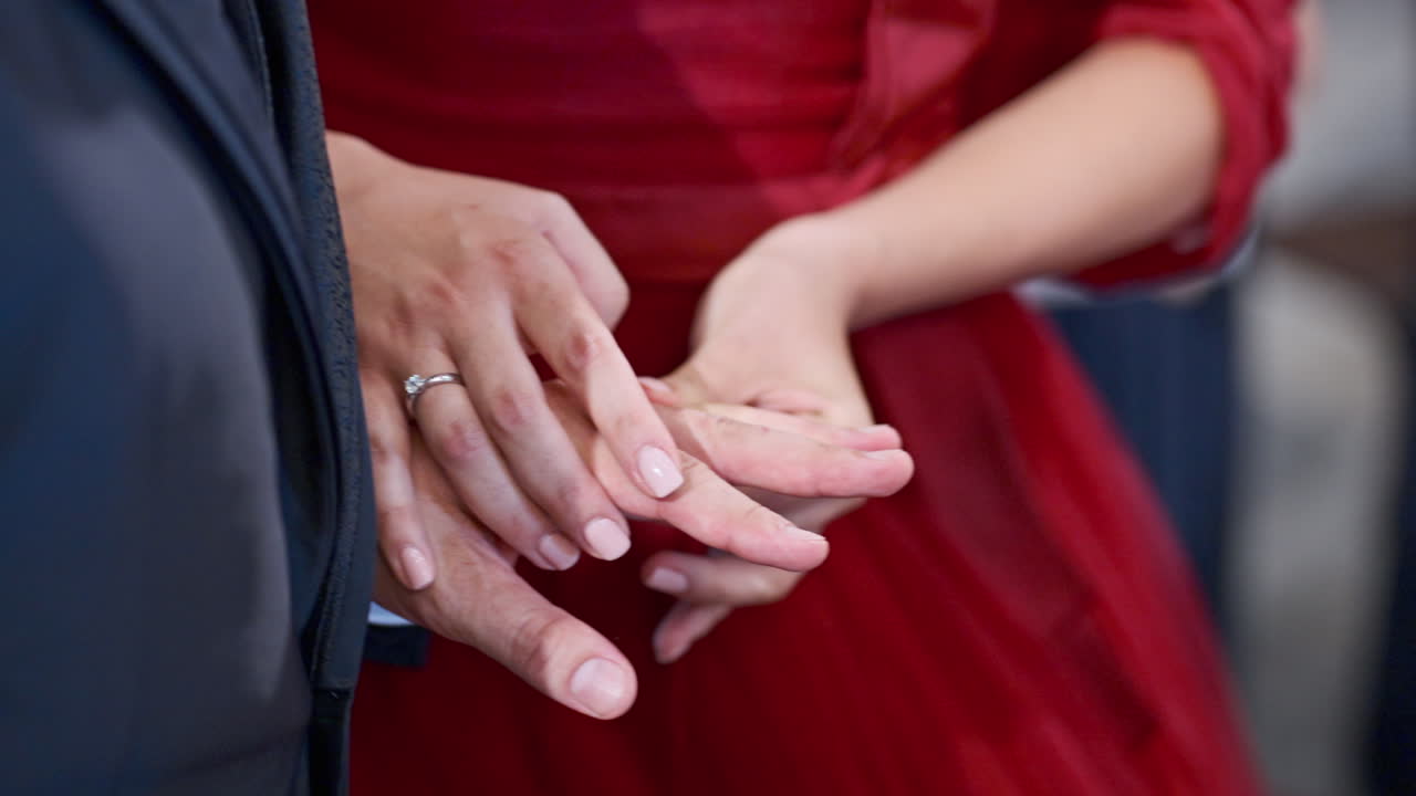 Close up of bride on red dress putting ring on groom on weeding, handheld