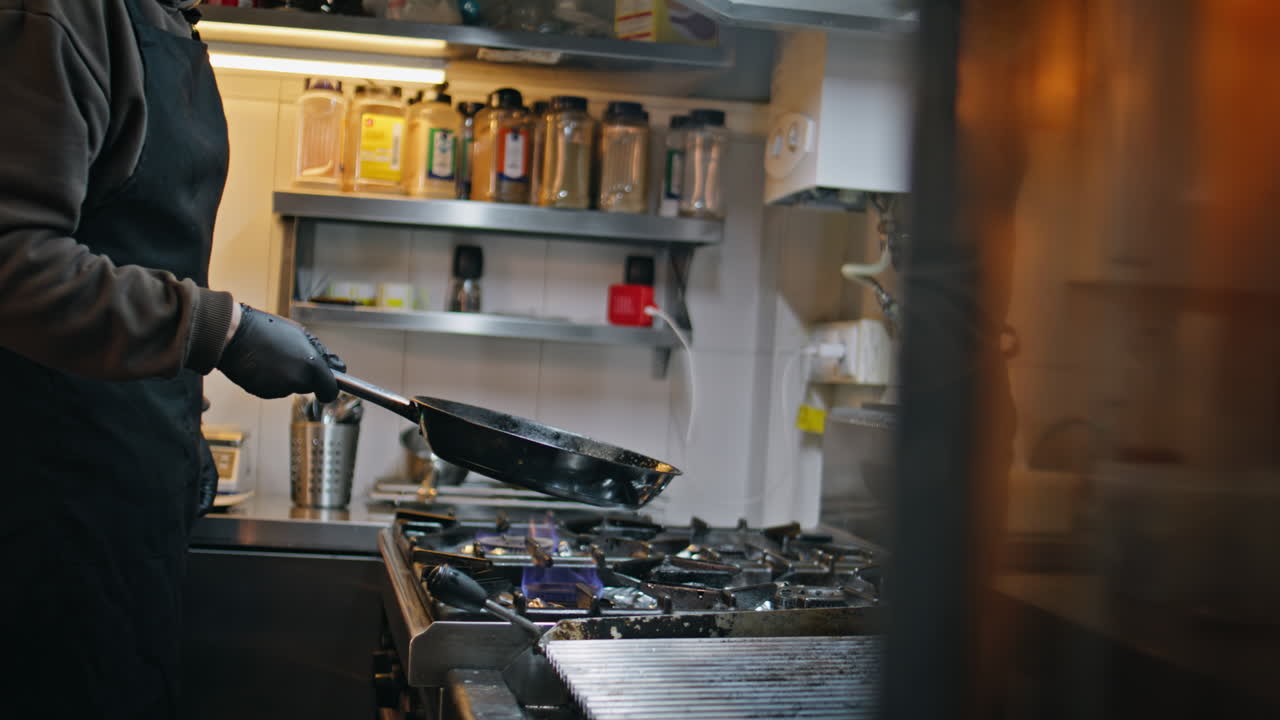 Chef working frying pan on gas stove kitchen workspace closeup. Unknown man