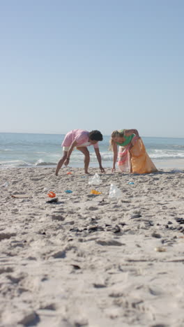 vertical video: cleaning beach, group of friends picking up trash from sand near ocean