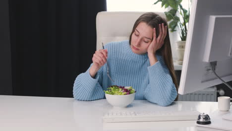 unhappy woman sitting at desk and eating healthy salad