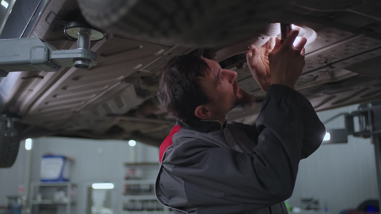 hombre mecánico automático mira debajo del coche levantado en el ascensor en busca de fallas en cámara lenta