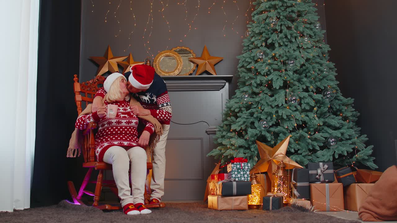 una pareja de ancianos celebra la navidad. el abuelo cubre con una manta a la abuela. la mujer bebe té.