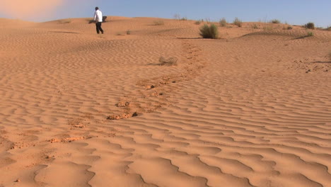 El-Hombre-Camina-Por-El-Desierto,-Una-Pequeña-Tormenta-De-Arena-Silba-Cerca-De-él