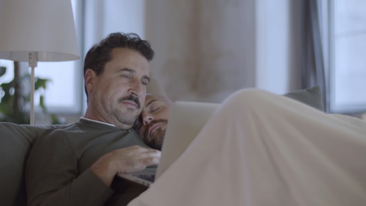 gay lindo acostado en la cama con su amante y mirando la pantalla de su portátil