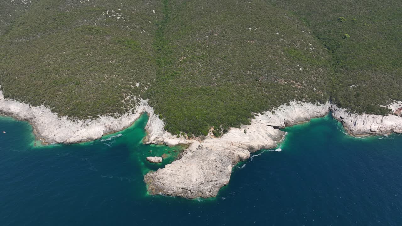 White rocky shoreline with turquoise water inlets and dense green hillside near Dugi Otok, Croatia. Aerial orbit from bird’s eye view
