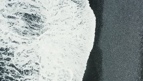 waves breaking on black sand beach reynisfjara in iceland, top down