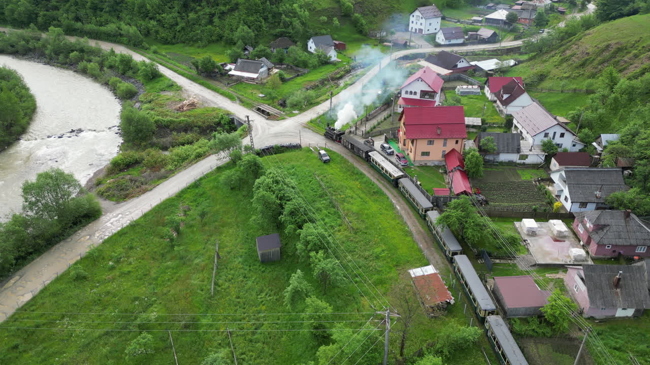 Aerial view of Mocanita steam train passing over a bridge in a picturesque Romanian village Viseu de Sus.