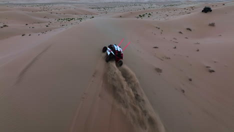 fpv drone shot following a atv quad riding on over dunes of the dubai desert