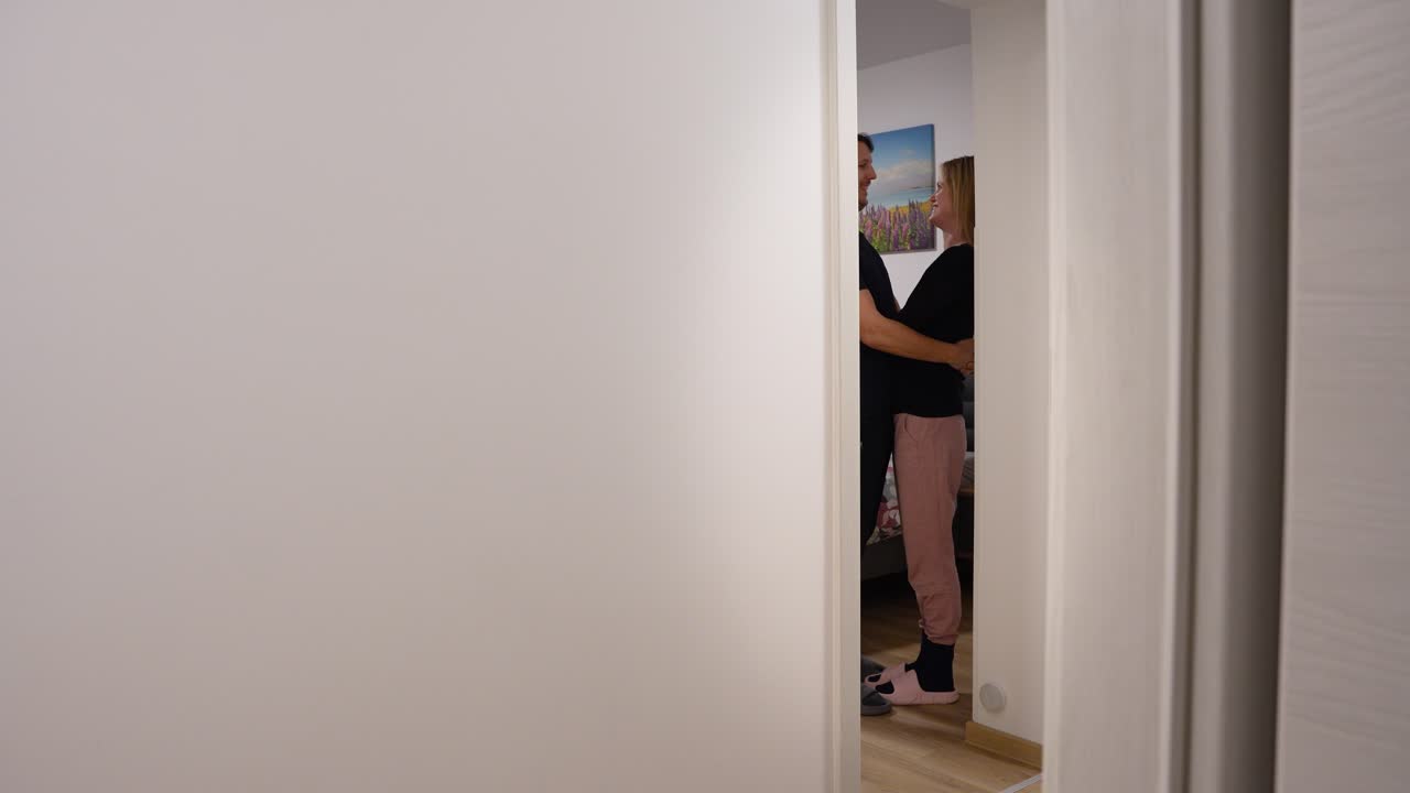 Couple shares a warm hug in a bedroom doorway at home
