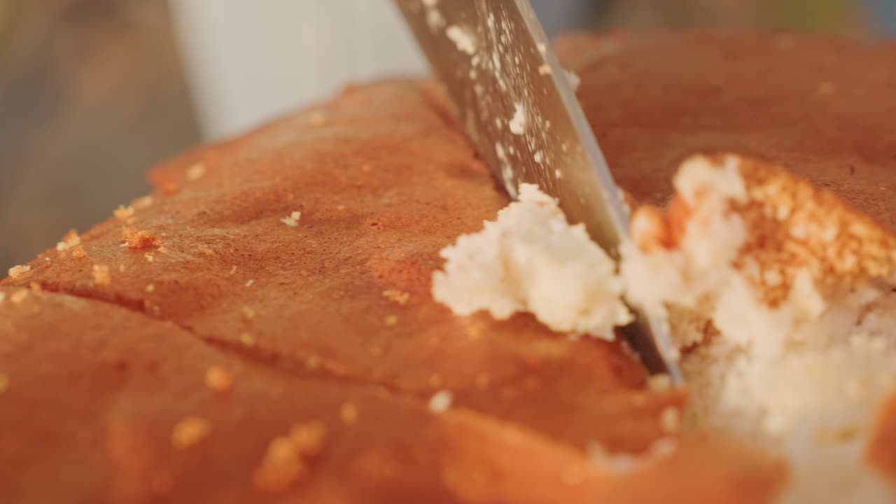 Camping cake closeup knife slice revealing soft crumb and moist interior, hands steadying knife, golden crust, crumbs falling, ASMR texture detail, camp table setting, evening light, intimate