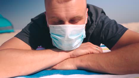 close up of man wearing a protective face mask laying on beach towel and standing up
