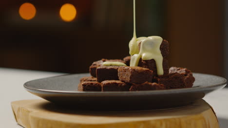 cerca de la salsa de chocolate blanco derretido que se vierte en la pila de brownies de chocolate en el plato