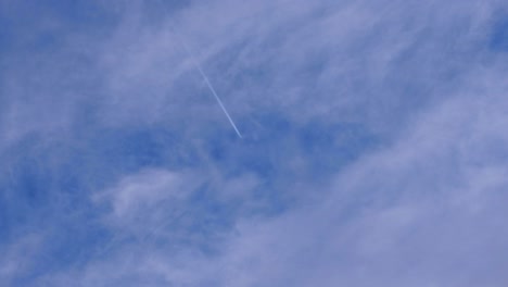 contrails and vapor trail lines from an aeroplane aircraft flying overhead against a fine blue, slightly cloudy sky