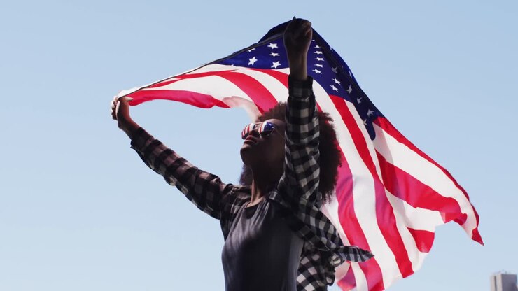 African american woman wearing sunglasses holding american flag up in the air