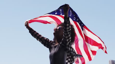 mujer afroamericana con gafas de sol sosteniendo la bandera estadounidense en el aire