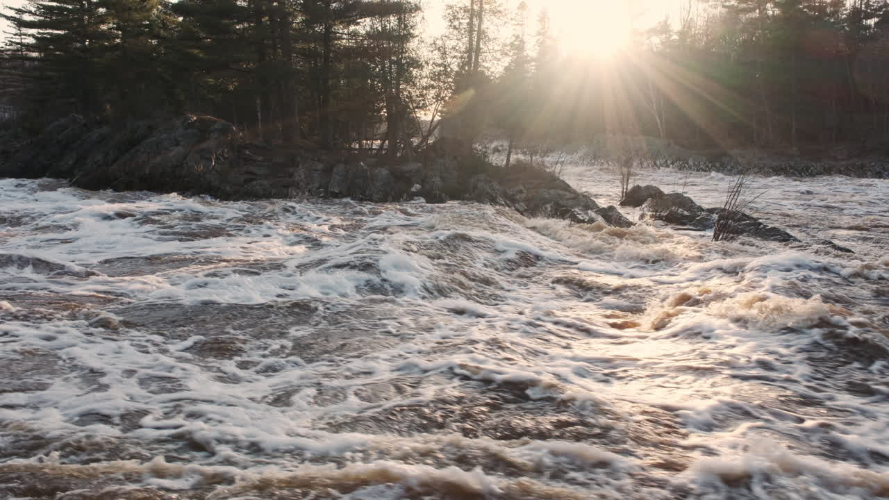 sonnenstrahlen werfen ein warmes leuchten auf einen brüllenden fluss, der mit dem frühlingsschnee schmilzt.