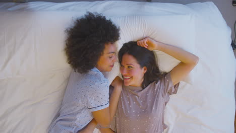 overhead shot of loving same sex female couple wearing pyjamas lying on bed at home