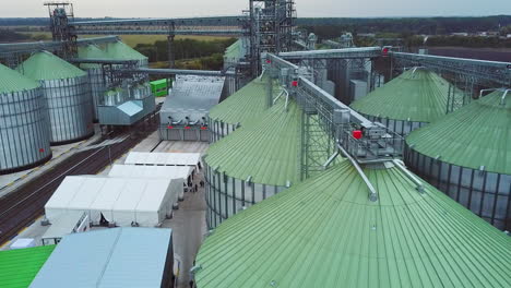 light green roofs of tanks joined by metal supports. railroad going through the plant territory and white tents nearby. top view.