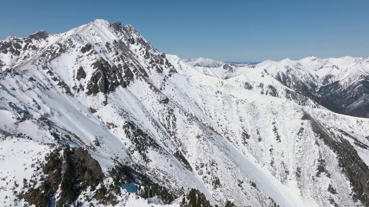 Filmato aereo del Picco Galina innevato e di una cresta montuosa frastagliata vicino al villaggio di Arshan, Repubblica di Buriazia, Russia, con cielo azzurro limpido e panorama alpino.