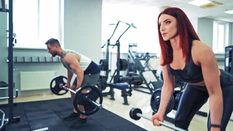 Persistent young couple training with metal barbell in sports club. Athletic woman and strong man lifting heavy weights on the background of modern simulators indoors.