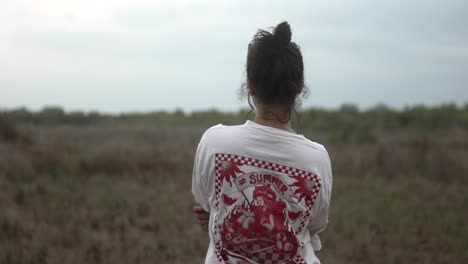 a woman stands in a field wearing a graphic t-shirt