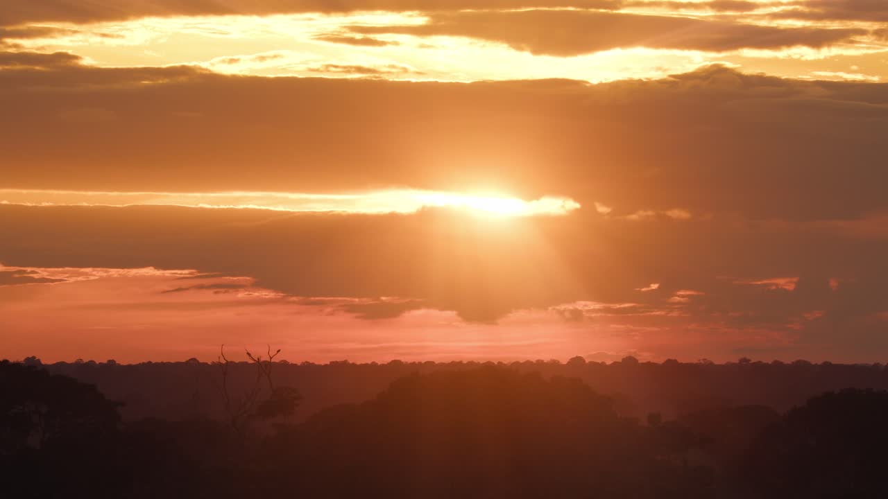 Very bright sun rays beam from behind dramatic clouds and then disappear during sunset above the amazon