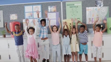 portrait of happy diverse schoolchildren raising hands over ecology texts at elementary school