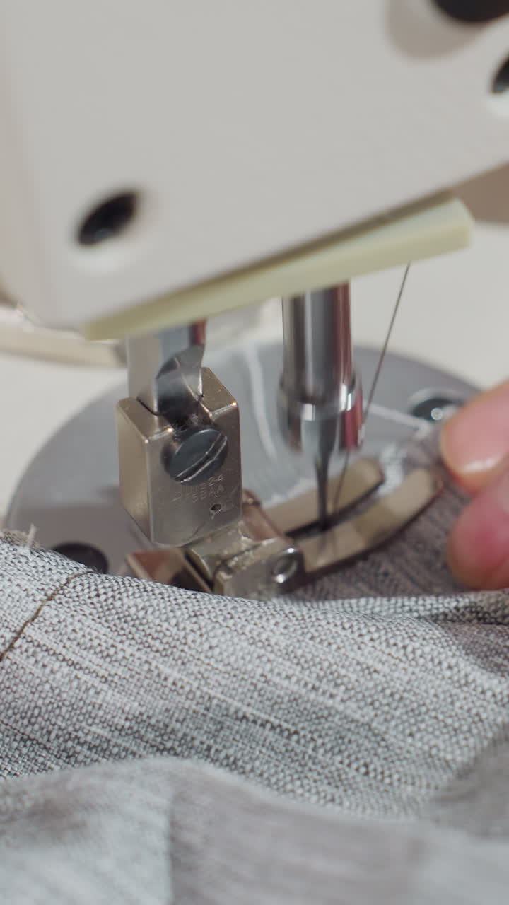 primer plano de costura de tela bajo el prensatelas, técnico guiando tela de punto con manos firmes, ajustes precisos de alimentación y tensión, acabado de costura para producción de prendas de vestir, placa de garganta metálica