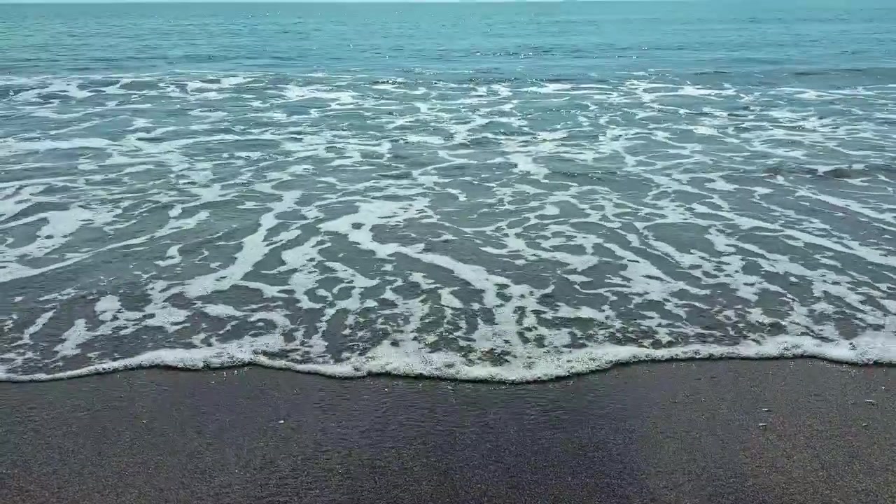 Onde si infrangono sulla riva mentre la luce del sole si riflette sull'acqua in una scena costiera di giorno