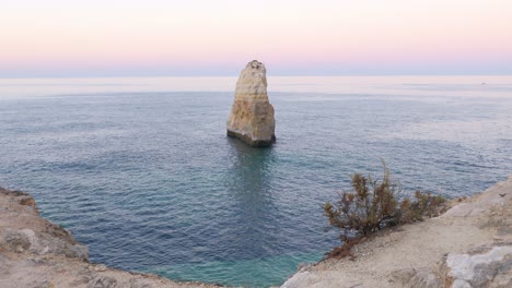 sunrise clifftop footage of a sea stack pillar on the algarve coast in portugal, slow pullback reveal of cliff edge