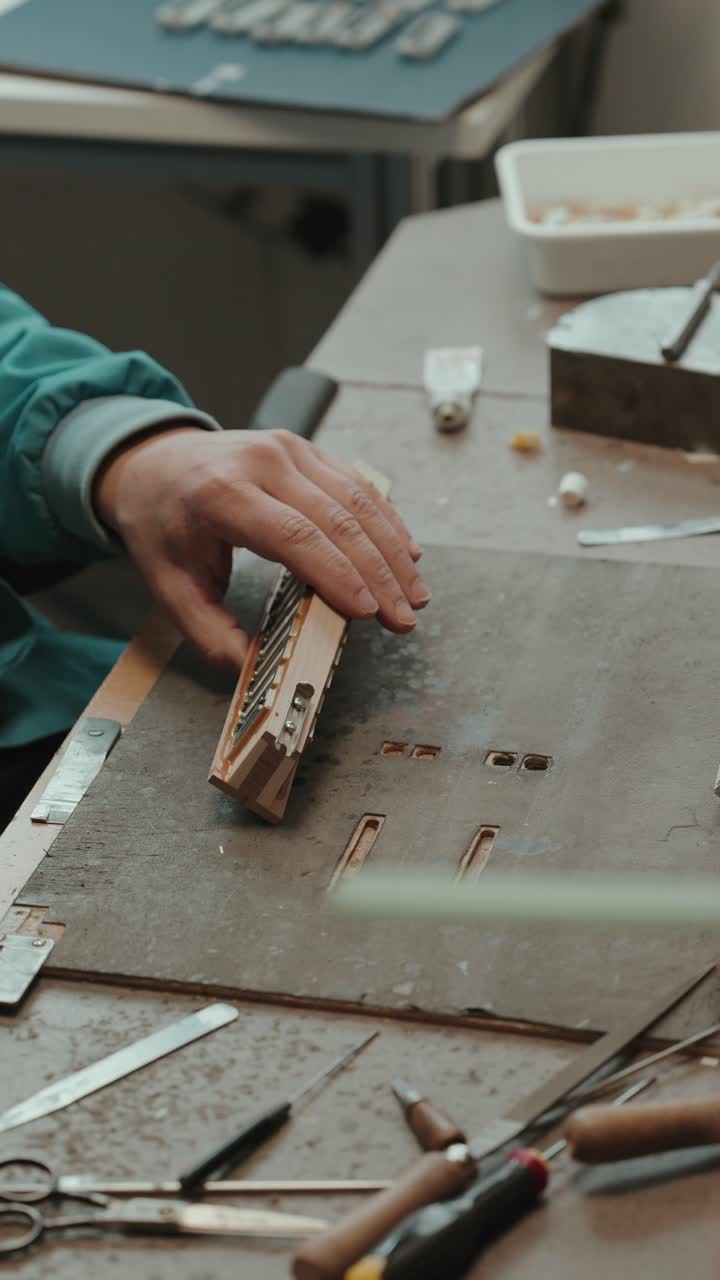 Hands repairing and adjusting concertina reed block on workbench with tools in Portugal workshop environment vertical